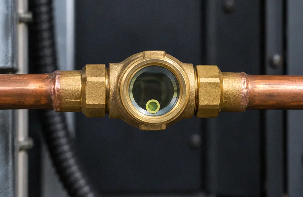 Brass refrigerant sight glass with a moisture indicator installed in a horizontal copper line.