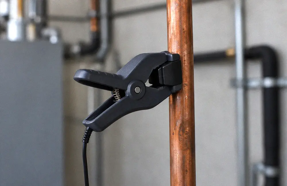 Wired pipe temperature clamp attached to a vertical copper refrigerant line.